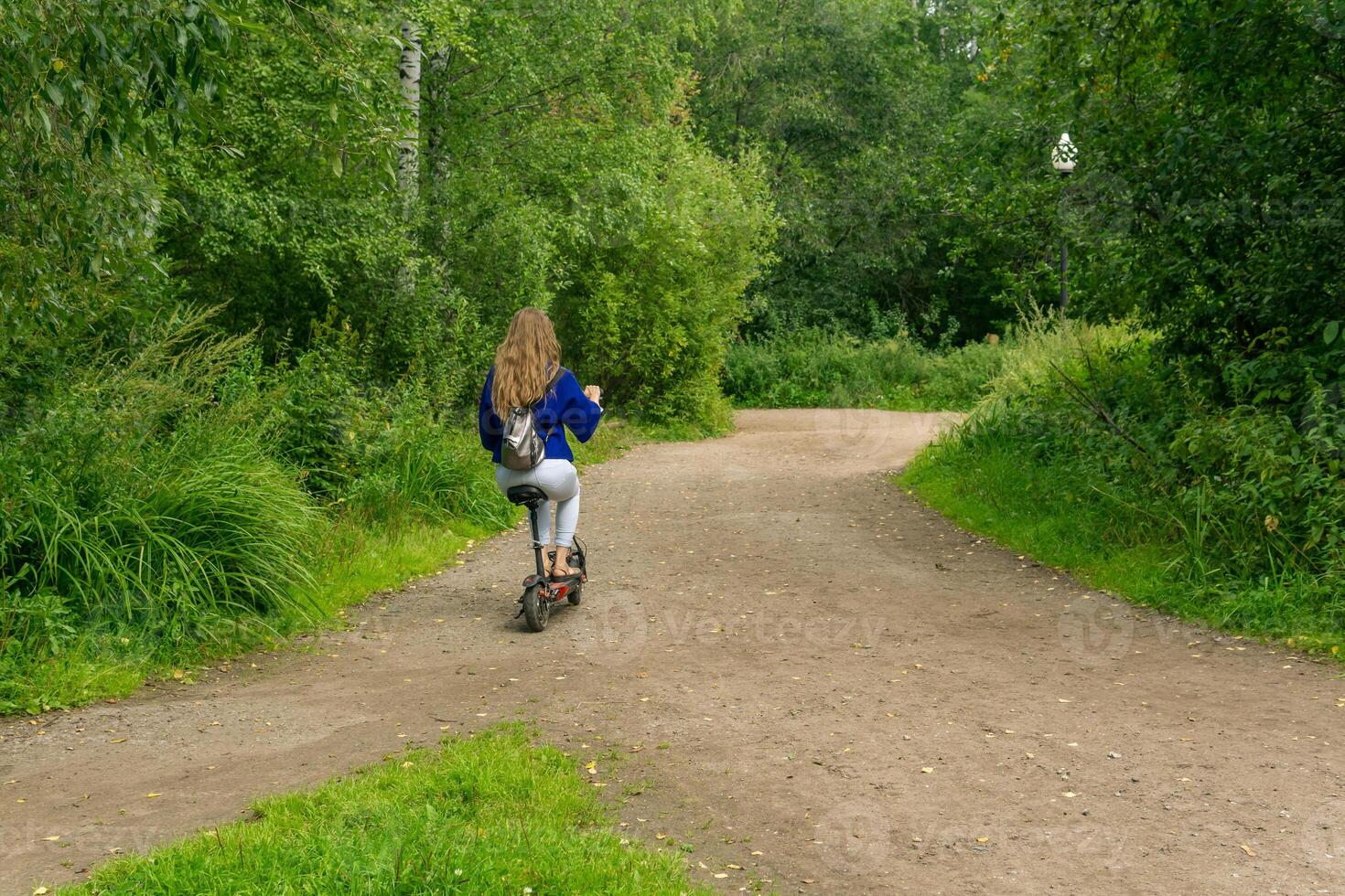 jong vrouw ritten een elektrisch scooter langs de pad in de park foto