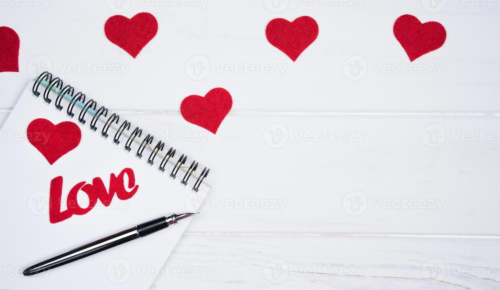 flatlay samenstelling met notitieboekje, pen en rood harten Aan een wit houten achtergrond. romantisch Gefeliciteerd naar Valentijnsdag dag. top visie. plaats voor tekst. foto