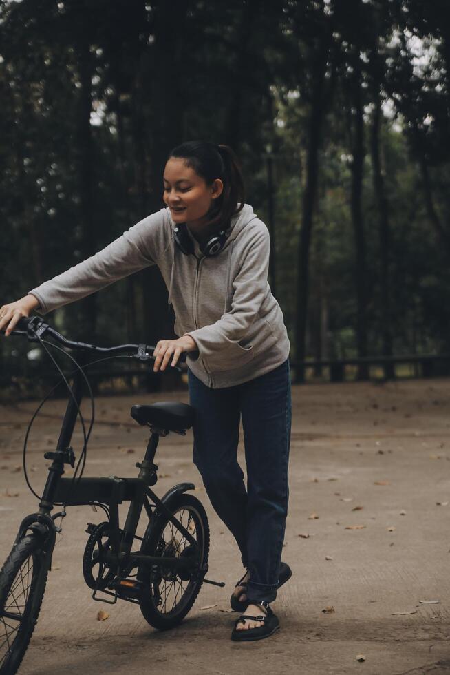 gelukkig Aziatisch jong vrouw wandelen en rijden fiets in park, straat stad haar glimlachen gebruik makend van fiets van vervoer, eco vriendelijk, mensen levensstijl concept. foto