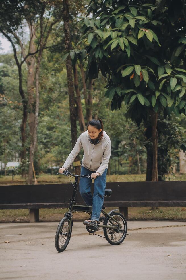 gelukkig Aziatisch jong vrouw wandelen en rijden fiets in park, straat stad haar glimlachen gebruik makend van fiets van vervoer, eco vriendelijk, mensen levensstijl concept. foto