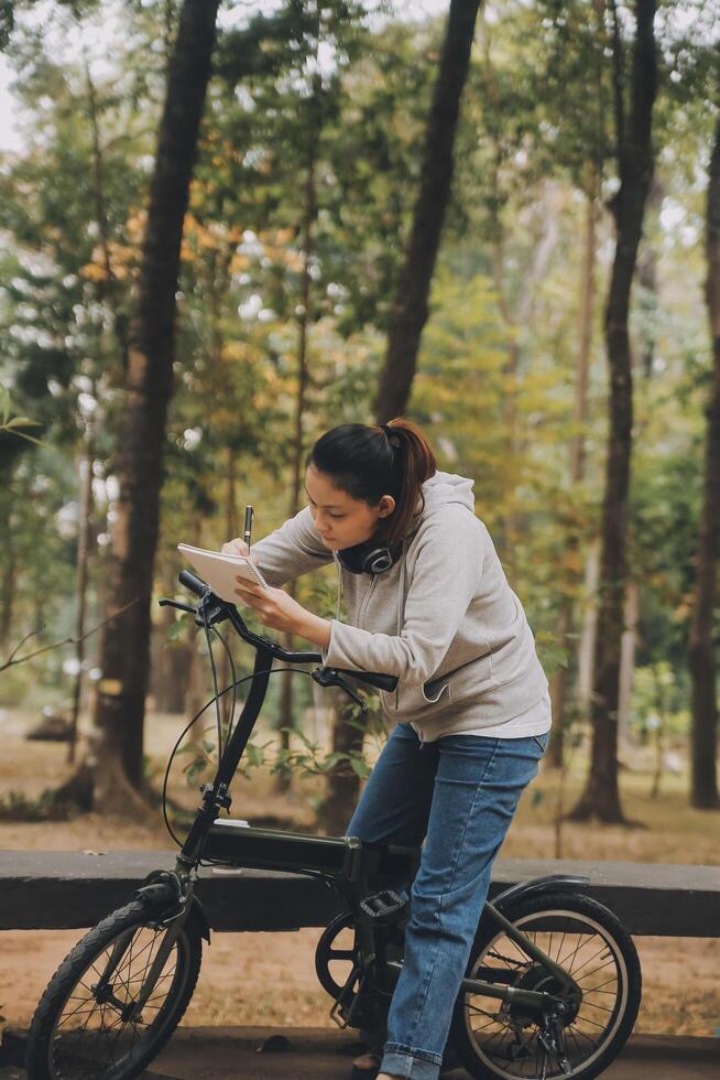 gelukkig Aziatisch jong vrouw wandelen en rijden fiets in park, straat stad haar glimlachen gebruik makend van fiets van vervoer, eco vriendelijk, mensen levensstijl concept. foto