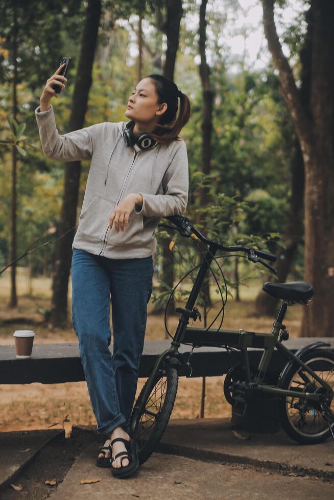 gelukkig Aziatisch jong vrouw wandelen en rijden fiets in park, straat stad haar glimlachen gebruik makend van fiets van vervoer, eco vriendelijk, mensen levensstijl concept. foto