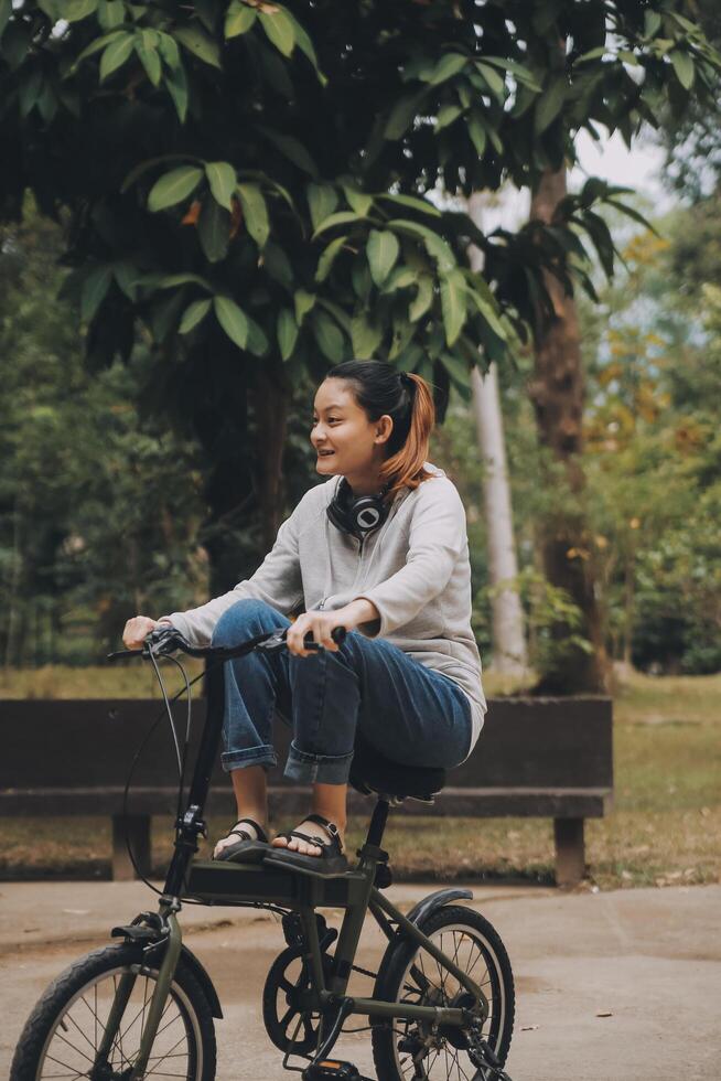 gelukkig Aziatisch jong vrouw wandelen en rijden fiets in park, straat stad haar glimlachen gebruik makend van fiets van vervoer, eco vriendelijk, mensen levensstijl concept. foto