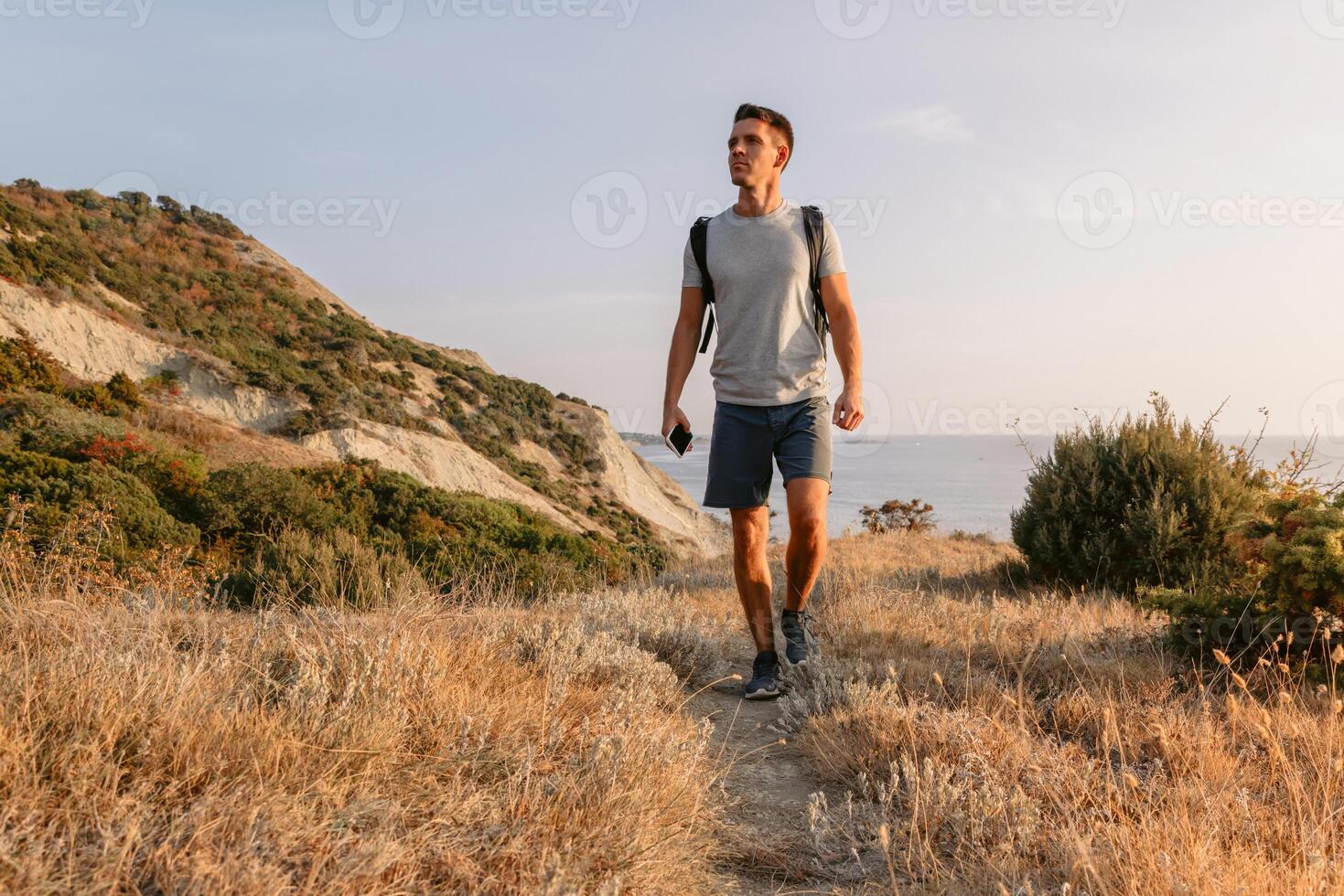knap Mens met rugzak wandelen Aan de oceaan kustlijn met bergen en avond warm zonlicht. foto