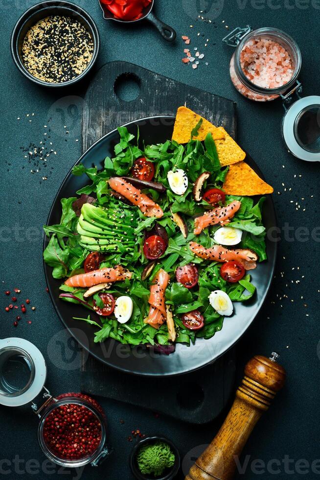 vers gezond salade. salade met rucola, gezouten Zalm, avocado, kwartel eieren en champignons. in een zwart bord. eetpatroon voedsel. foto