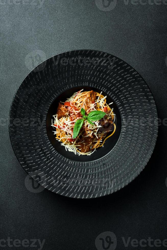 pasta met kalfsvlees, tomaten en kaas in een zwart schaal. Aan een donker achtergrond, detailopname. foto