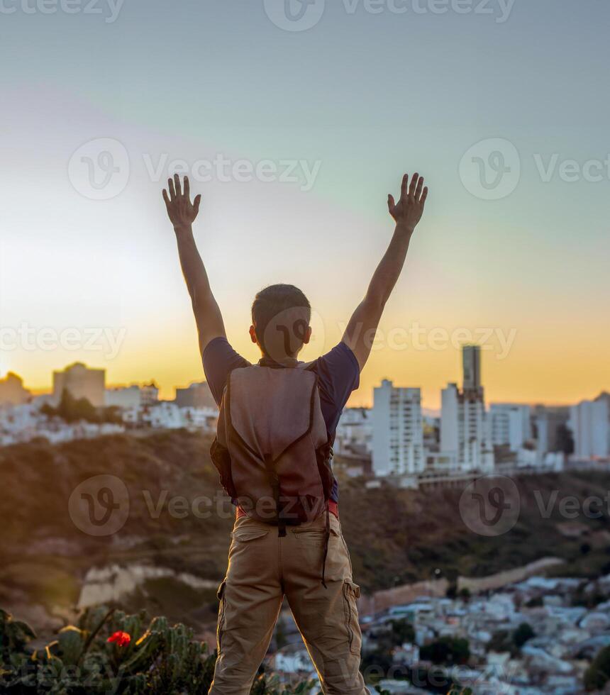 bevoegd jong Mens verhogen zijn handen naar de lucht Aan een zonsondergang hoog bovenstaand de stad foto