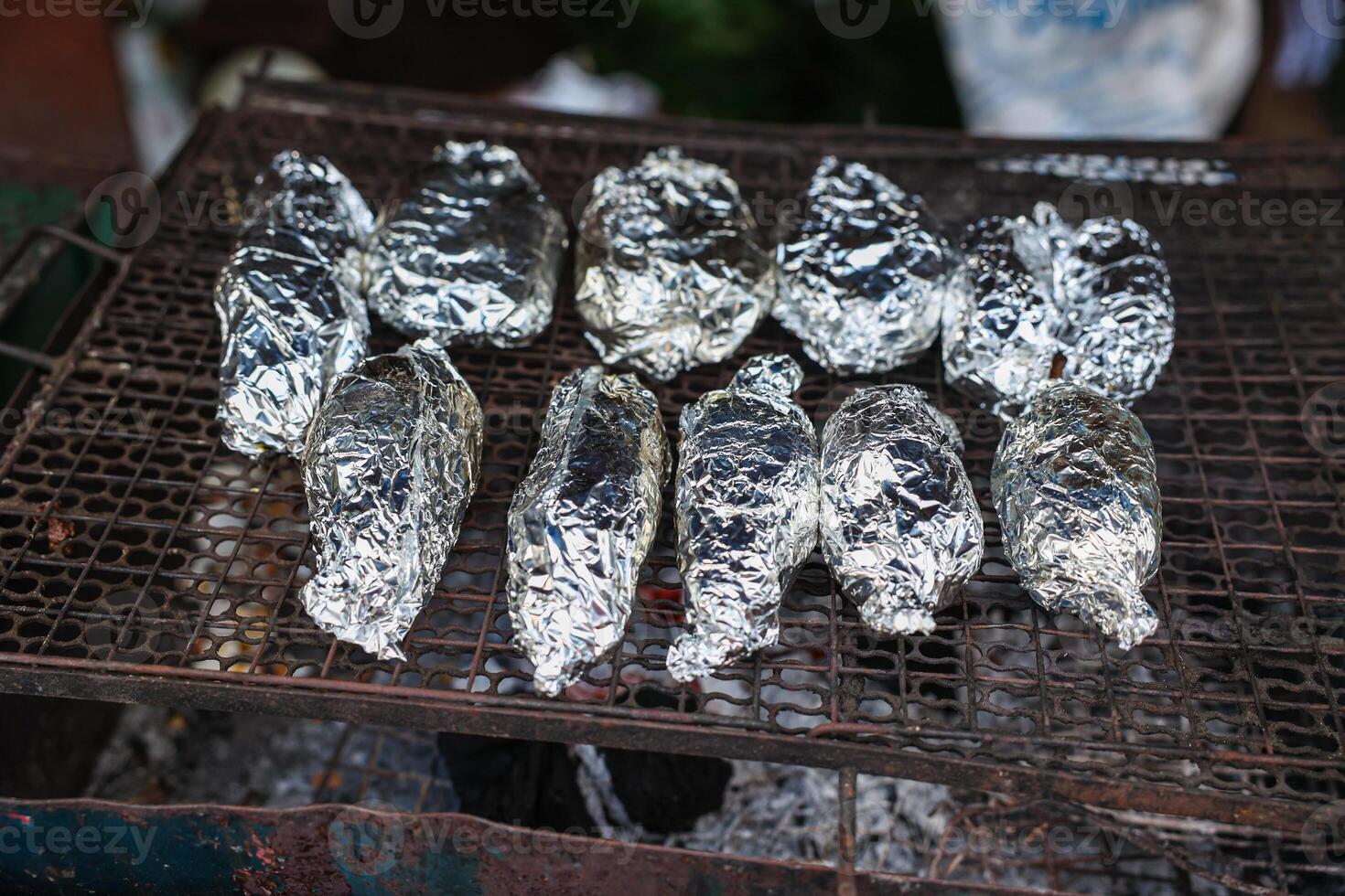 vis of aardappel verpakt aan het bedekken met aluminium folie papier grillen Aan houtskool fornuis foto