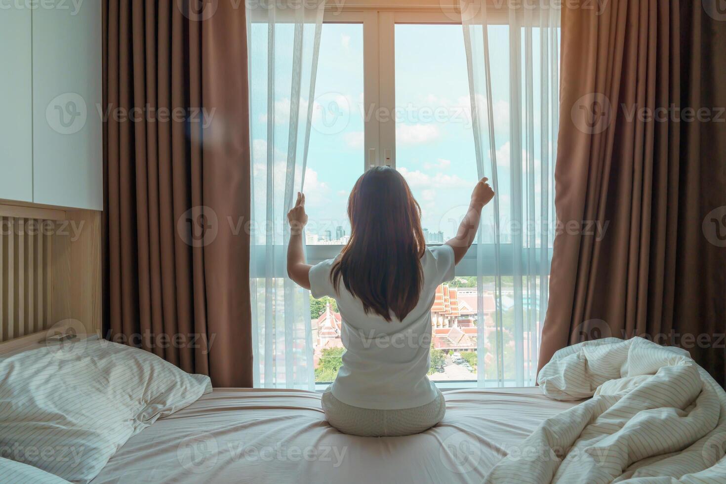 gelukkig vrouw uitrekken Aan bed na wakker worden omhoog, jong volwassen vrouw stijgende lijn armen en op zoek naar venster in de vroeg ochtend. vers kom tot rust en hebben een mooi hoor dag concepten foto