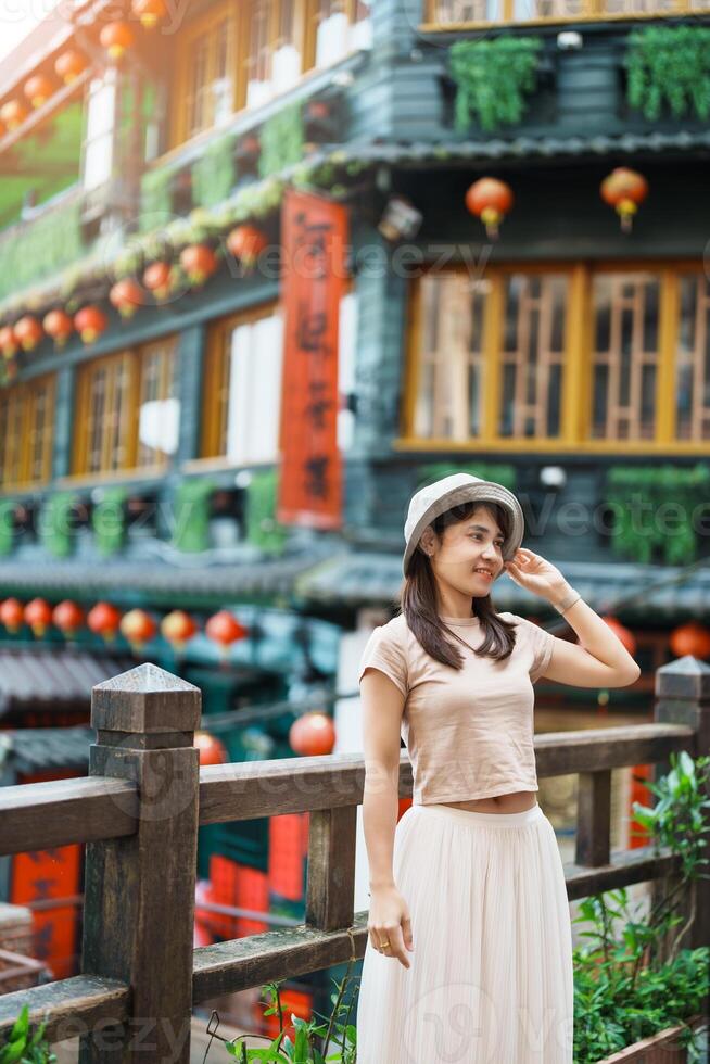 vrouw reiziger bezoekende in Taiwan, toerist met hoed bezienswaardigheden bekijken in jiufen oud straat dorp met thee huis achtergrond. mijlpaal en populair attracties in de buurt Taipei stad . reizen en vakantie concept foto