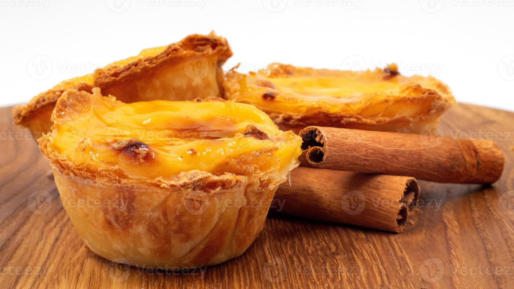 drie pastel de nata of Portugees ei scherp en kaneel stokjes Aan een houten bruin achtergrond. pastel de belem is een klein nagerecht, een bekervormig gebakje gemaakt van bladerdeeg gebakje met vla. foto