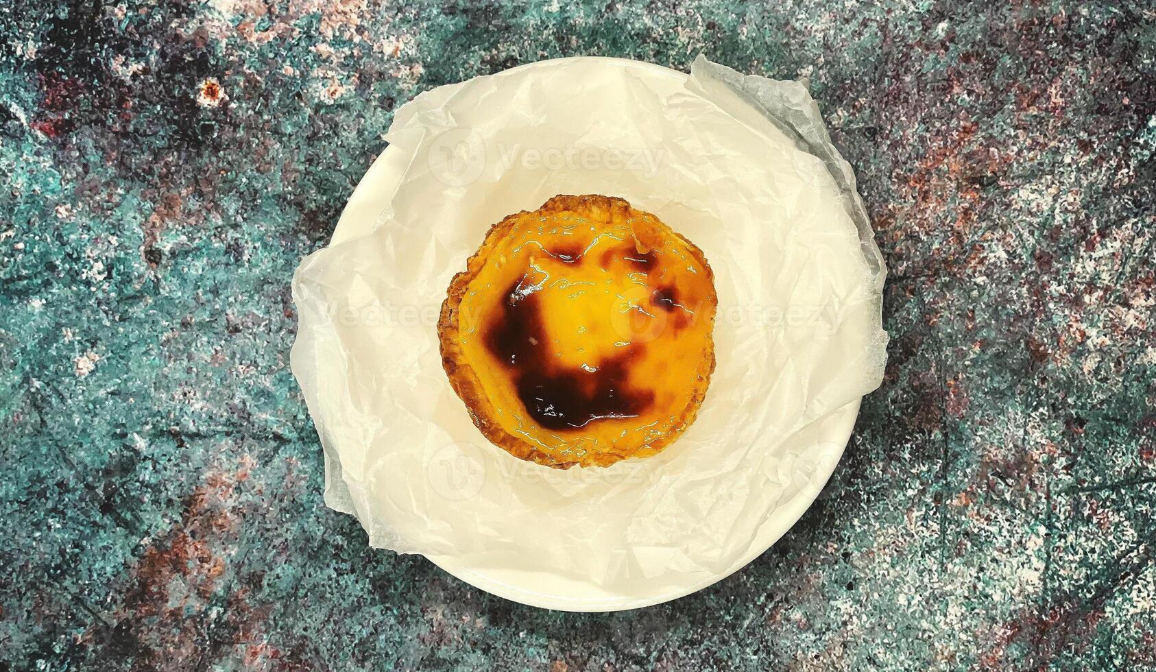 een pastel de nata of Portugees ei scherp Aan een wit bord. pastel de bel is een klein taart met een krokant bladerdeeg gebakje korst en een vla room vulling. foto