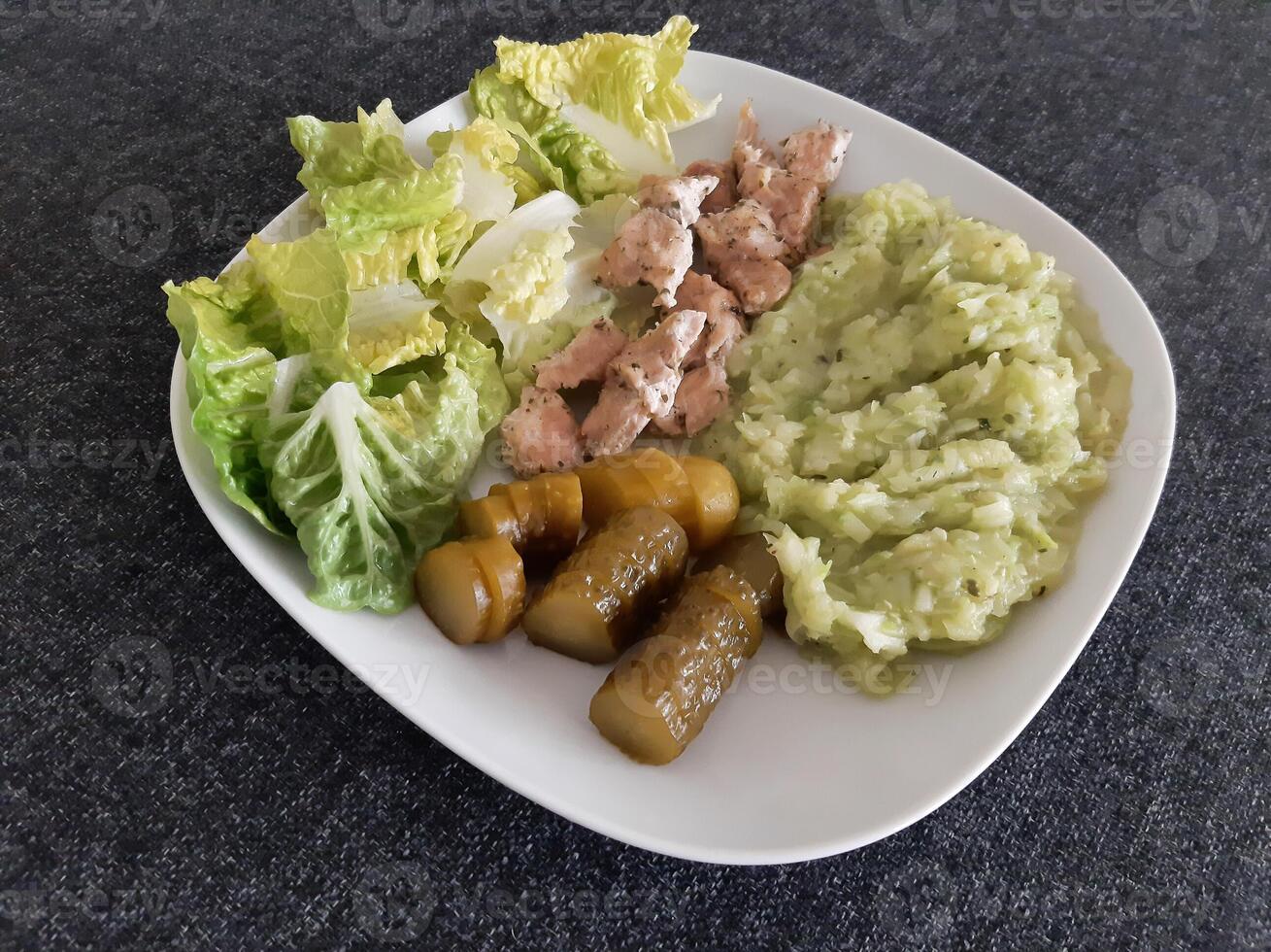 eigengemaakt gegrild kip met courgette stoofpot, groen salade en komkommer augurken geserveerd Aan een wit bord foto