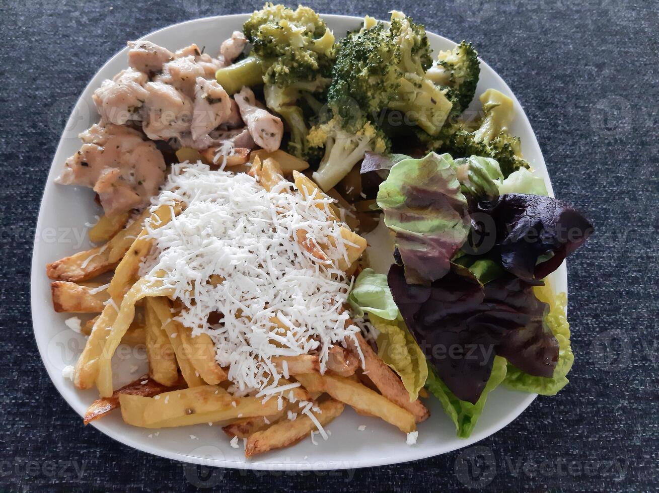 eigengemaakt gegrild kip met Frans Patat, broccoli, kaas en groen salade, geserveerd Aan een wit bord foto