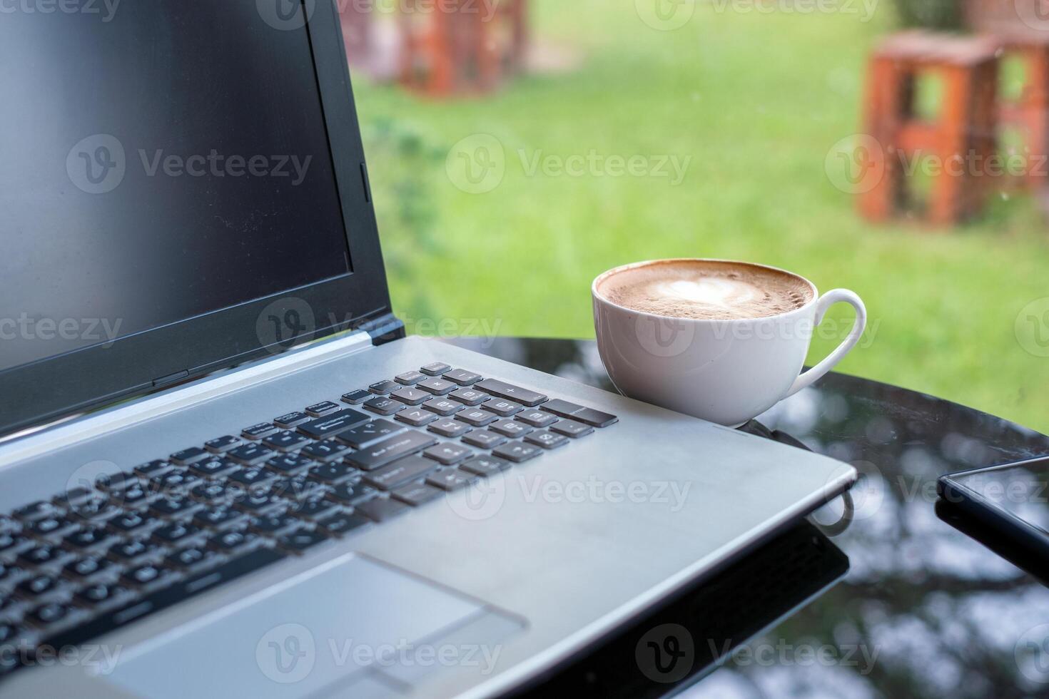 laptop met latte heet koffie in wit kop Aan glas tafel foto