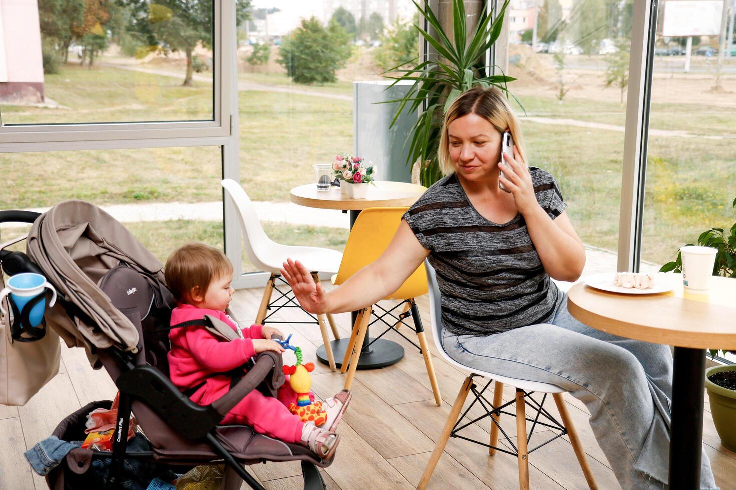 vrouw met een kind in een wandelwagen in een cafe praat Aan de telefoon Bij de dezelfde tijd vermaakt de kind foto