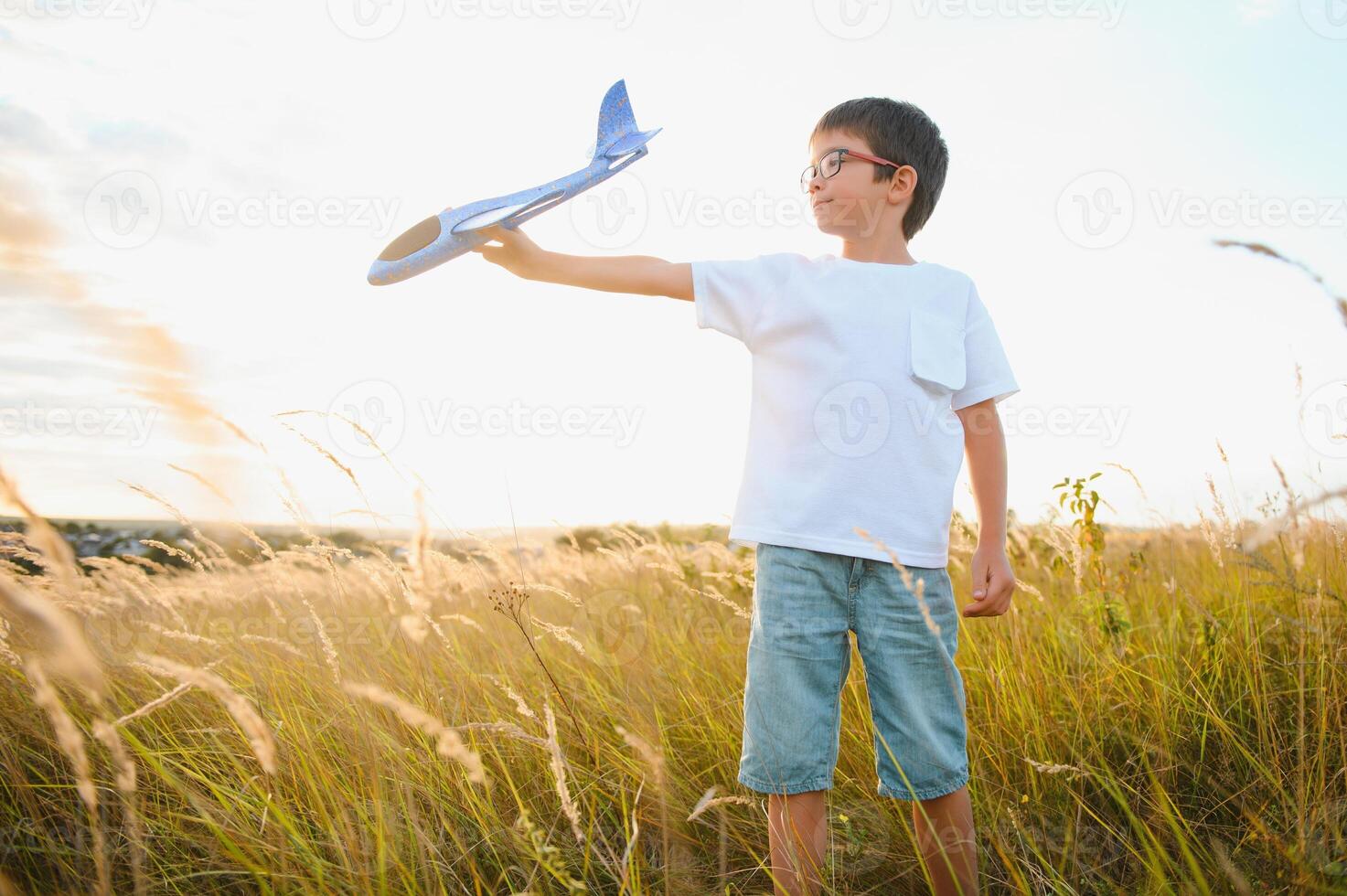 de kind loopt met een speelgoed- vlak. zoon dromen van vliegen. gelukkig kind, jongen, loopt Aan de zon spelen met een speelgoed- vliegtuig Aan de zomer veld- foto