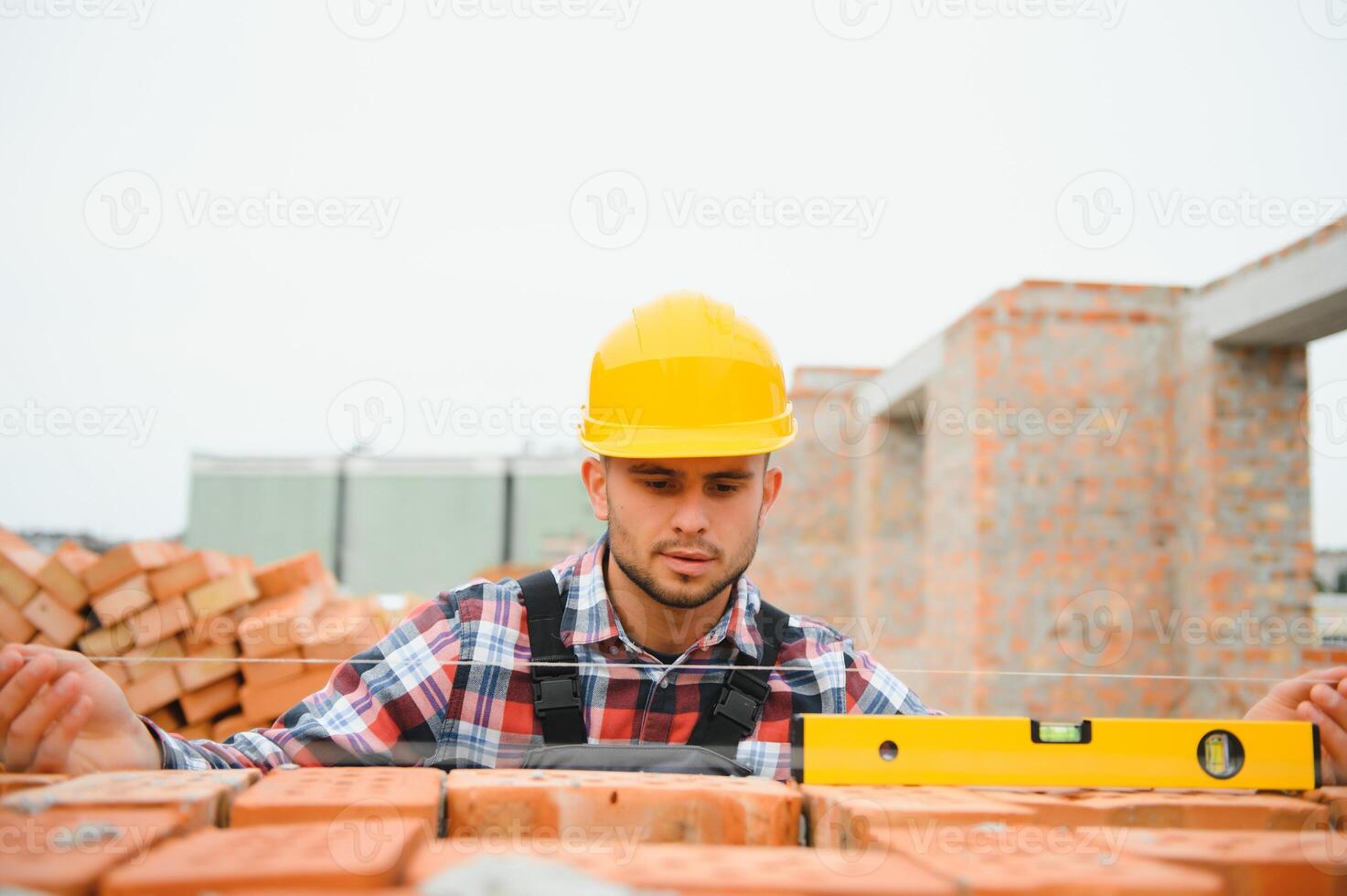 installeren steen muur. bouw arbeider in uniform en veiligheid uitrusting hebben baan Aan gebouw foto