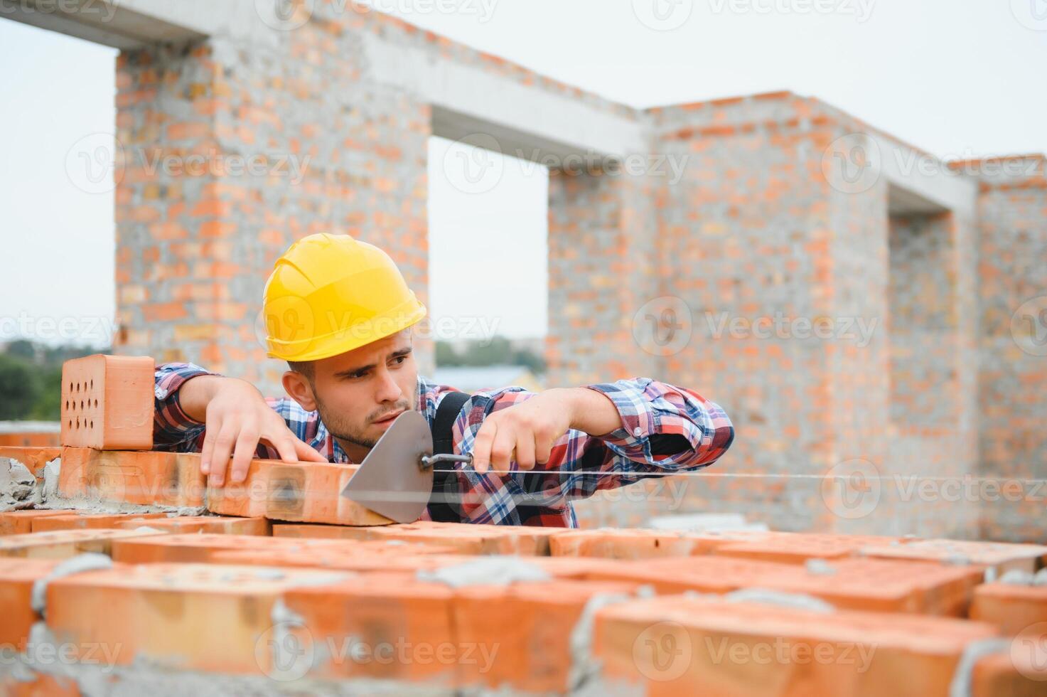 bezig met steen muur. bouw arbeider in uniform en veiligheid uitrusting hebben baan Aan gebouw. foto