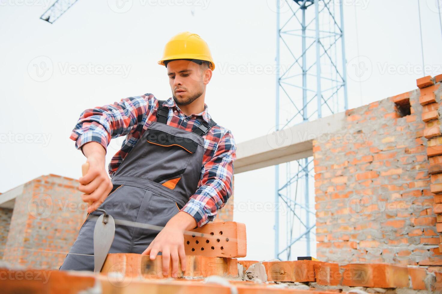 bezig met steen muur. bouw arbeider in uniform en veiligheid uitrusting hebben baan Aan gebouw. foto