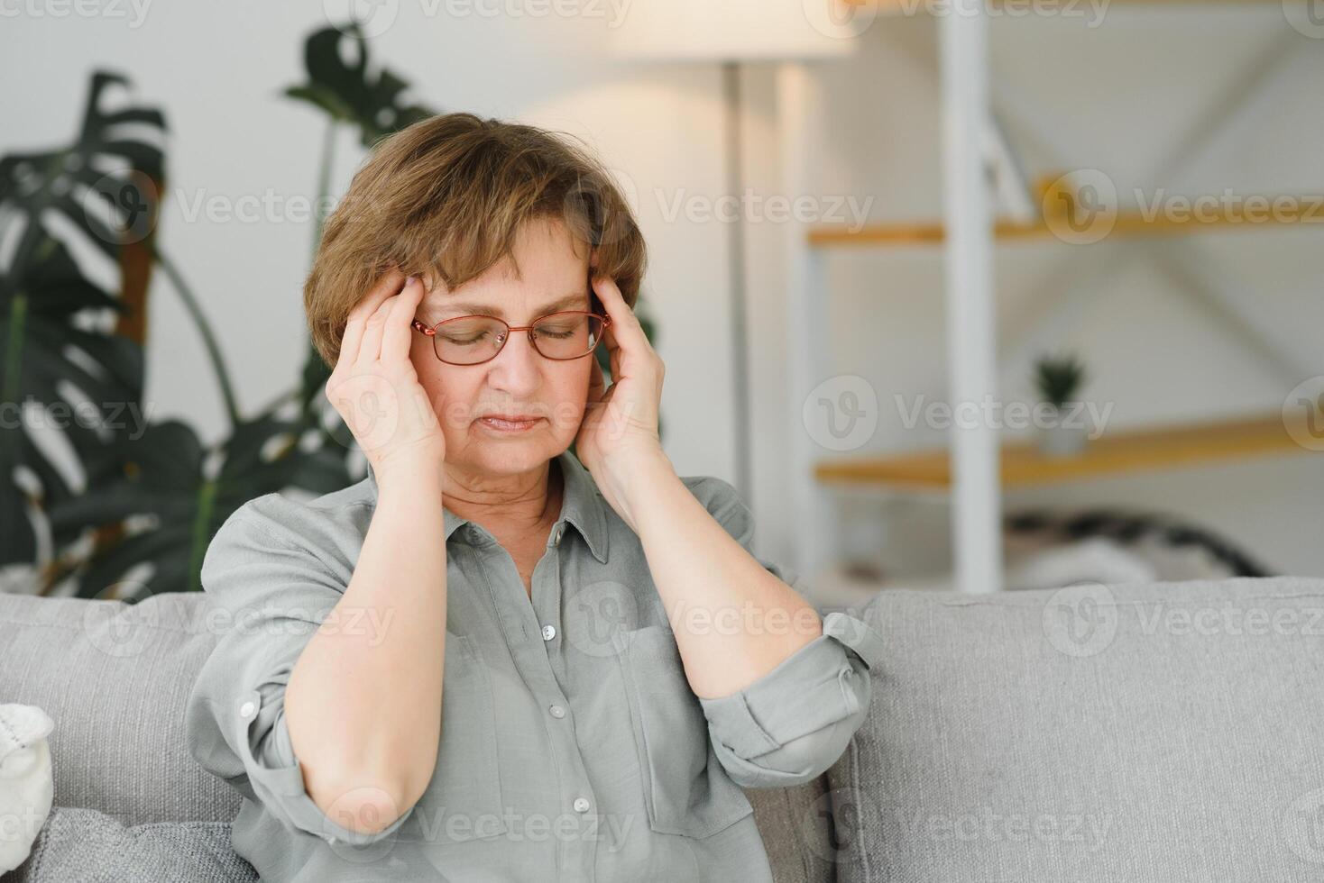 ouderen senior vrouw masseren haar tempels naar verminderen haar hoofdpijn. ouder dame gevoel bang, gespannen, en denken van ziekte of mentaal Gezondheid terwijl lijden van een erge, ernstige migraine of geheugen verlies foto