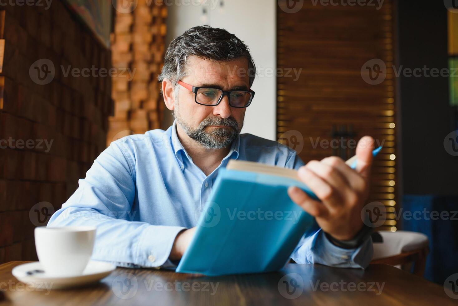 senior oud Mens lezing een boek in een koffie winkel, genieten van zijn literair hobby foto