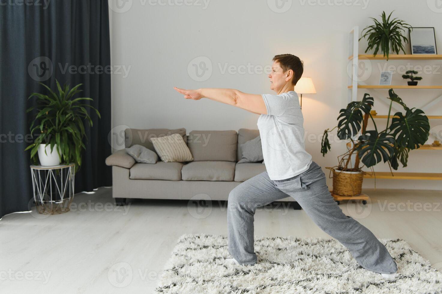 volwassen vrouw aan het doen geschiktheid opdrachten Bij huis. senior vrouw Doen uitrekken opdrachten. volwassen vrouw aan het doen yoga poses foto