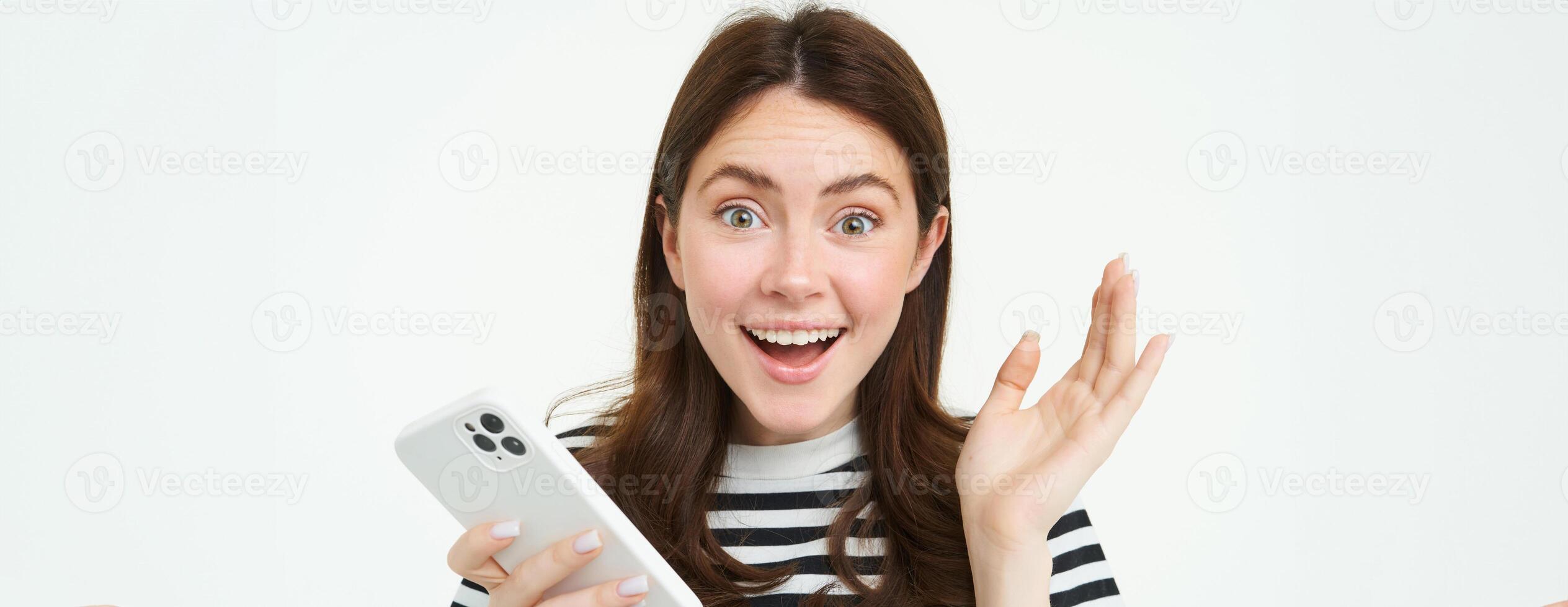 portret van Vrolijk, verrast jong vrouw, Holding mobiel telefoon, tonen versteld staan reactie naar Super goed nieuws, staand met smartphone over- wit achtergrond foto