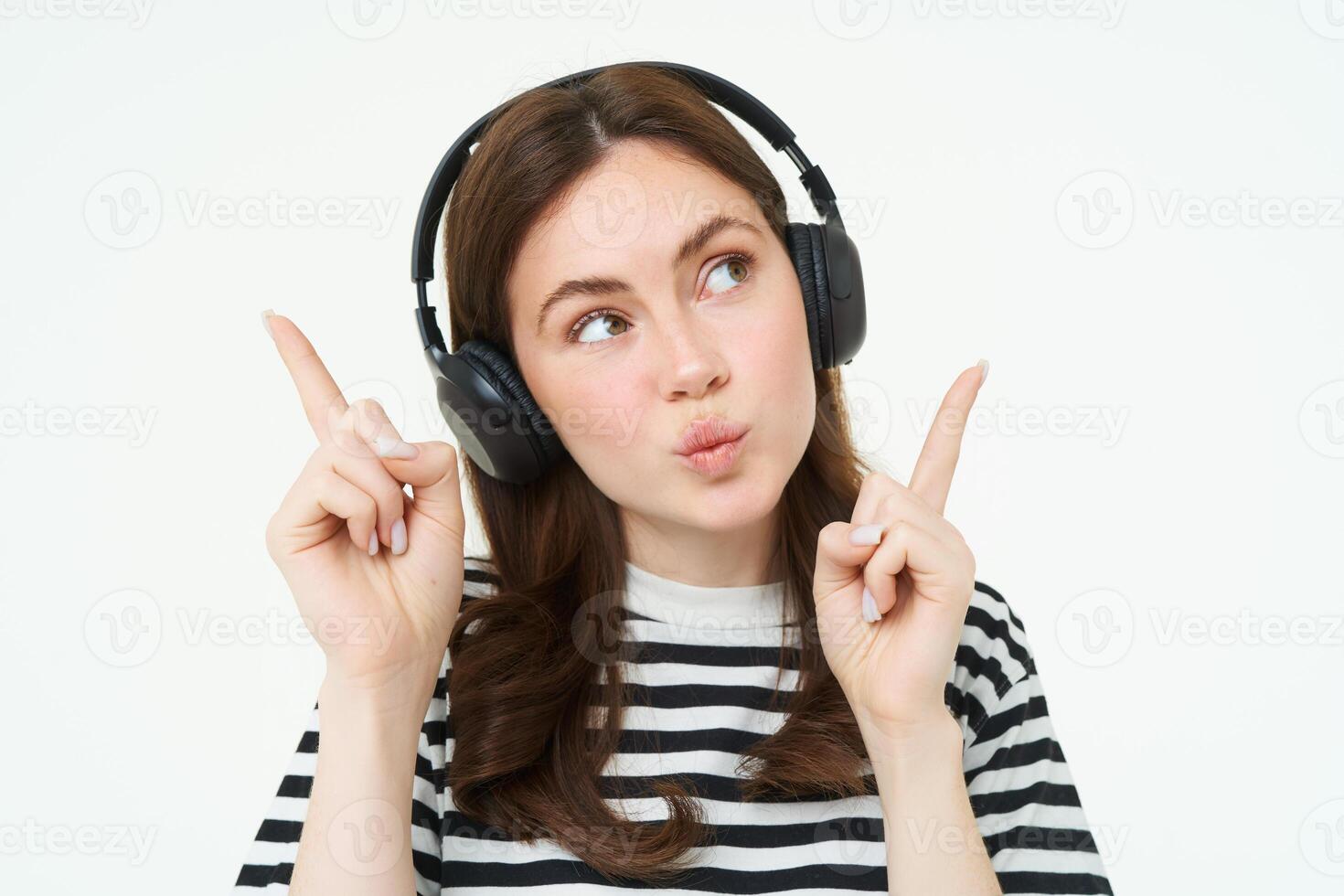 portret van jong brunette vrouw in koptelefoon, luisteren muziek- in koptelefoon, richten vingers omhoog, tonen banier, advertentie, geïsoleerd over- wit achtergrond foto