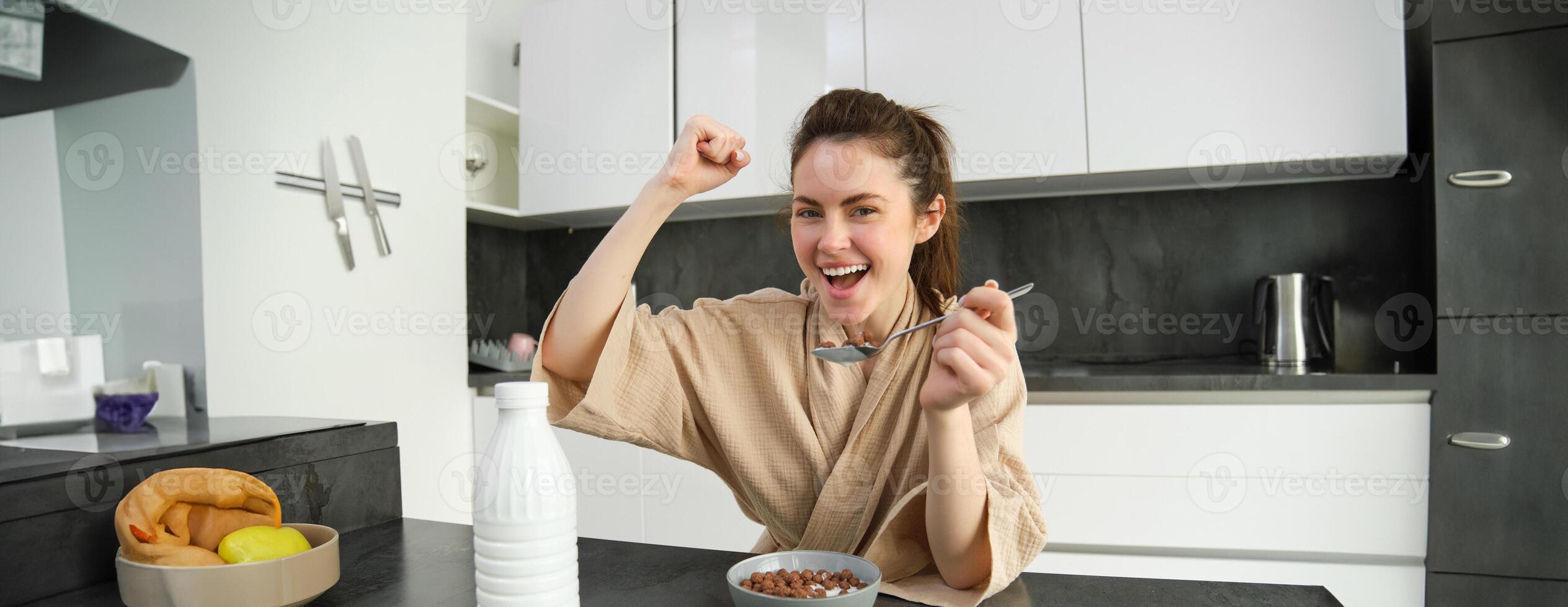 portret van Vrolijk, lachend jong vrouw aan het eten granen met melk, zegevierend, hebben ontbijt en gevoel opgewonden, energiek ochtend- concept foto