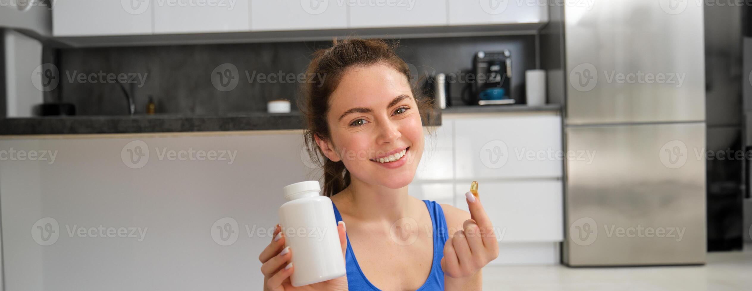 gelukkig jong fit meisje, aan het doen sport- Bij huis, shows dieet supplementen, nemen vitamines voor gezond lichaam, aanbevelen, tonen drug capsule foto