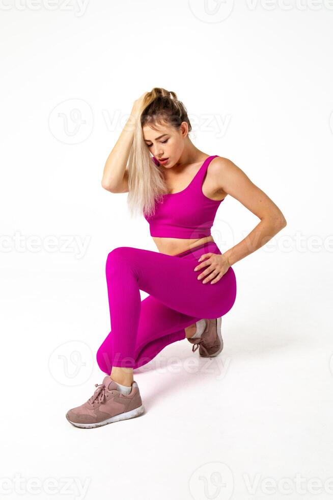 vrouw in levendig roze sport- kleding met een knie Aan verdieping en andere krom in voorkant en hand- in haren op zoek naar beneden foto