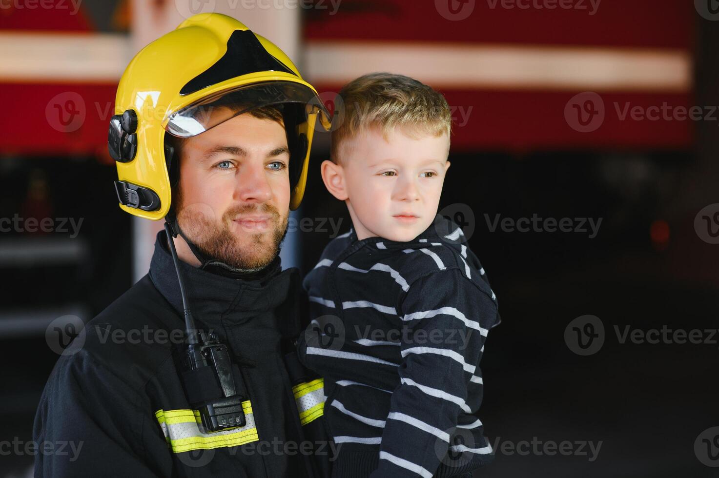 vuil brandweerman in uniform Holding weinig opgeslagen jongen staand Aan zwart achtergrond. foto