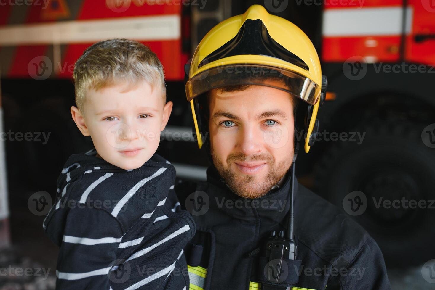 vuil brandweerman in uniform Holding weinig opgeslagen jongen staand Aan zwart achtergrond foto