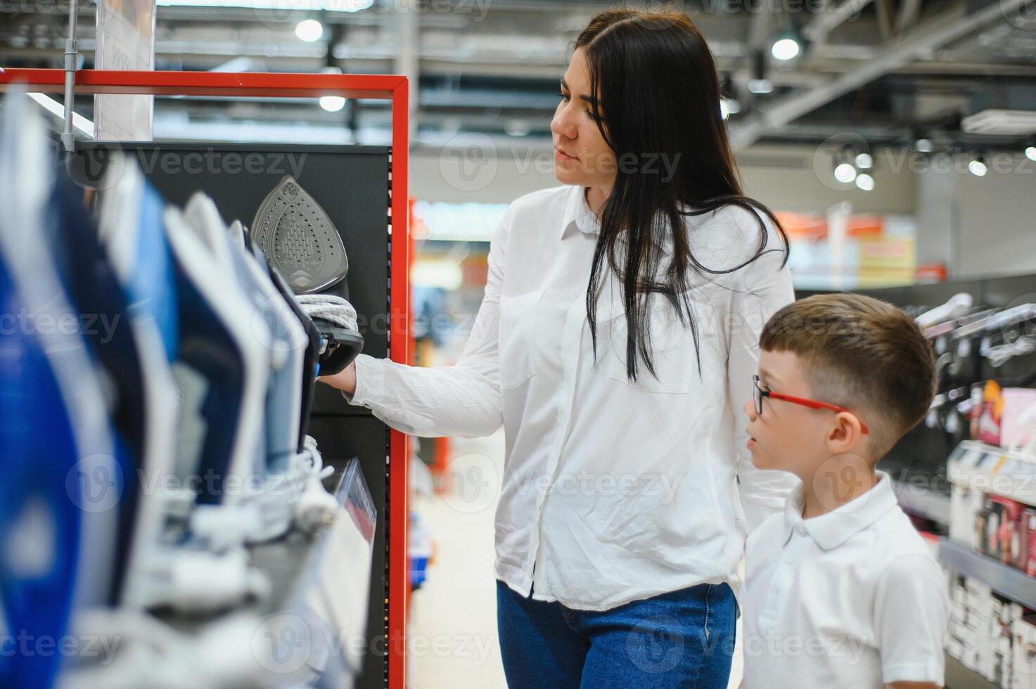 vrouw met zoon kiezen elektrisch ijzer in elektronica op te slaan foto