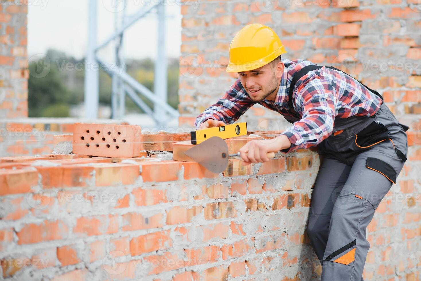 geel gekleurde moeilijk hoed. jong Mens werken in uniform Bij bouw Bij dag. foto