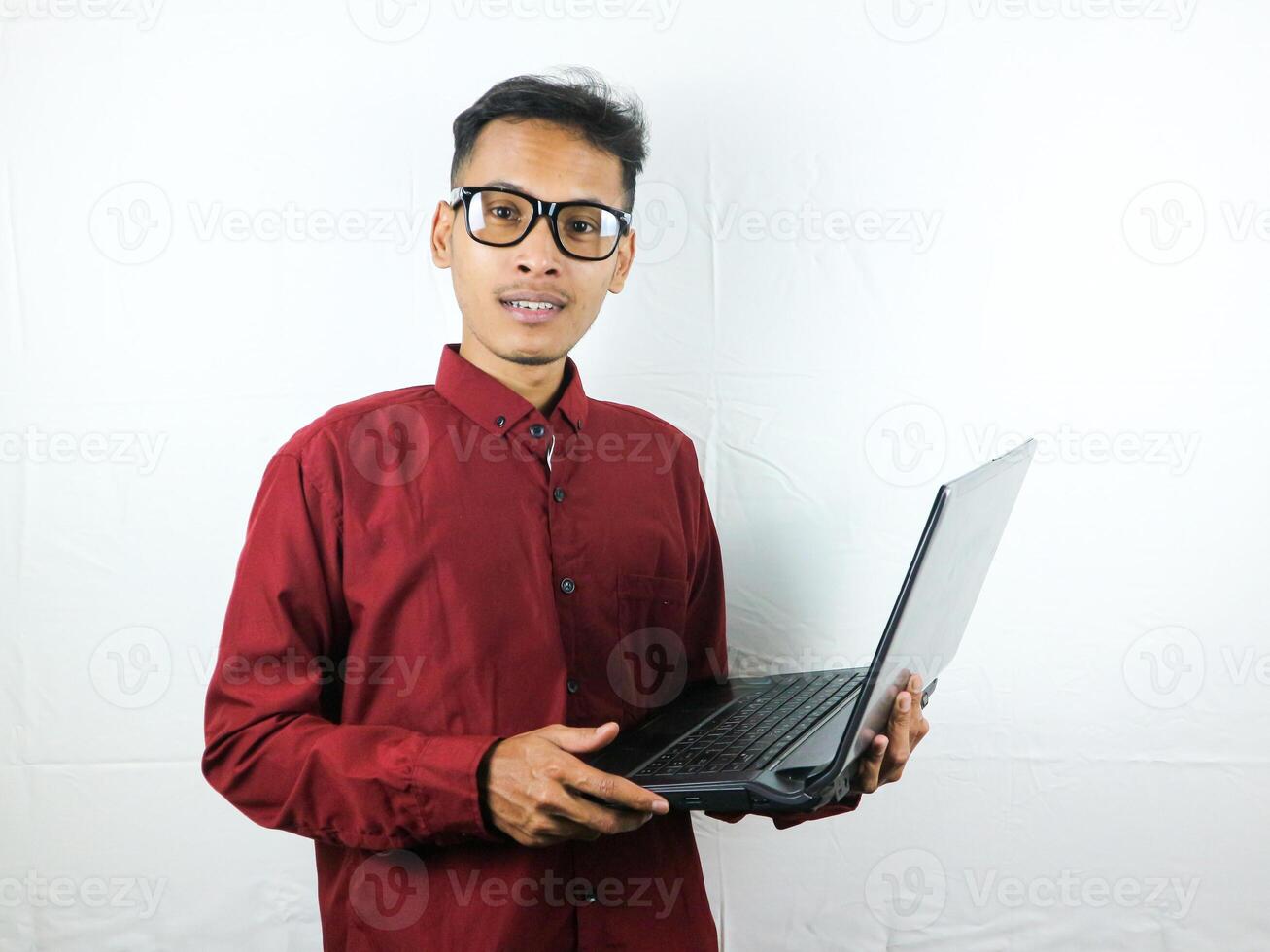 portret van een Aziatisch Mens vervelend een rood kleren Holding een laptop met een glimlachen gezicht uitdrukking. foto