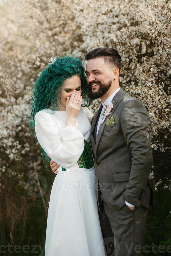 een gebaard bruidegom Toneelstukken en een meisje met groen haar- tegen de achtergrond van bloeiend voorjaar foto