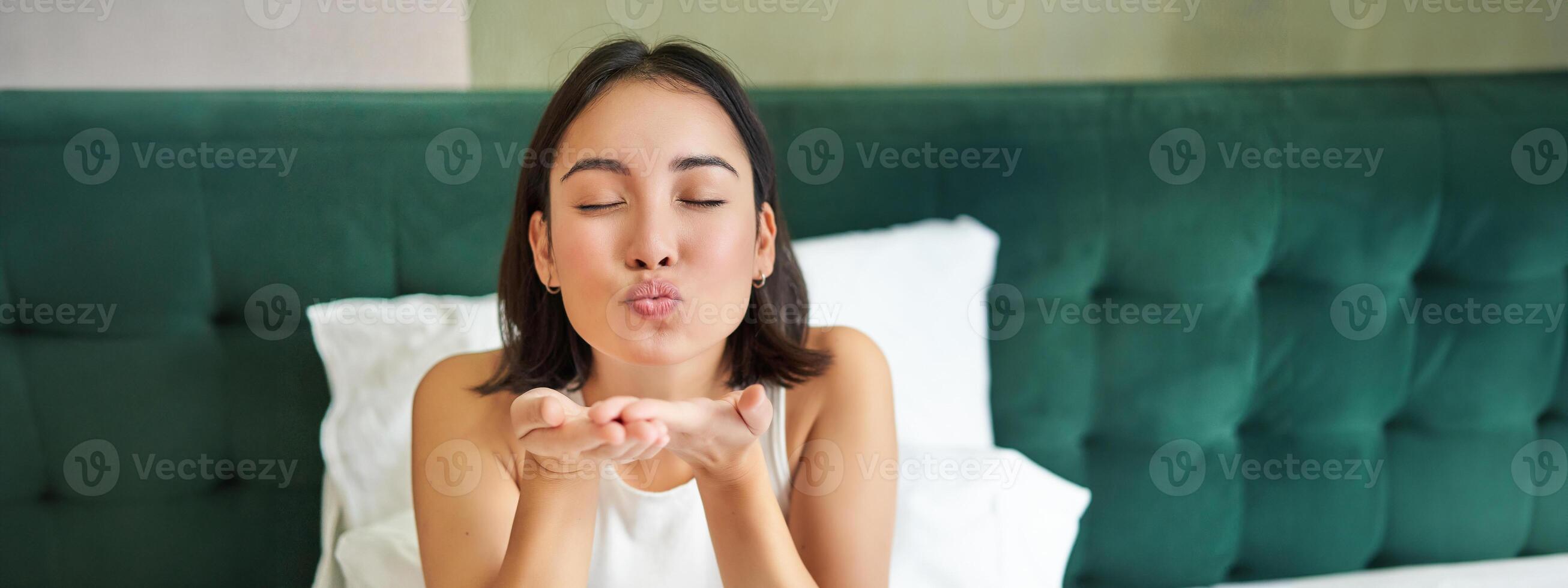 mooi Koreaans vriendin, meisje in bed, Bezig met verzenden lucht kus Bij camera, aan het liegen in bed in haar slaapkamer, ontwaken omhoog vroeg foto