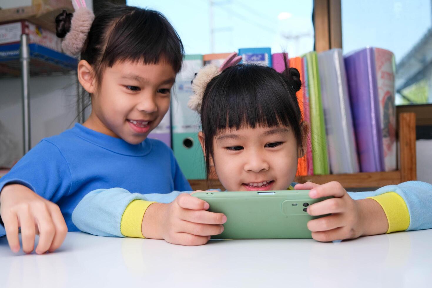 schattig weinig meisje Holding smartphone op zoek Bij scherm glimlachen gebruik makend van sollicitatie, spelen online spellen, aan het kijken tekenfilms in leven kamer Bij huis. kinderen en modern technologie concept foto