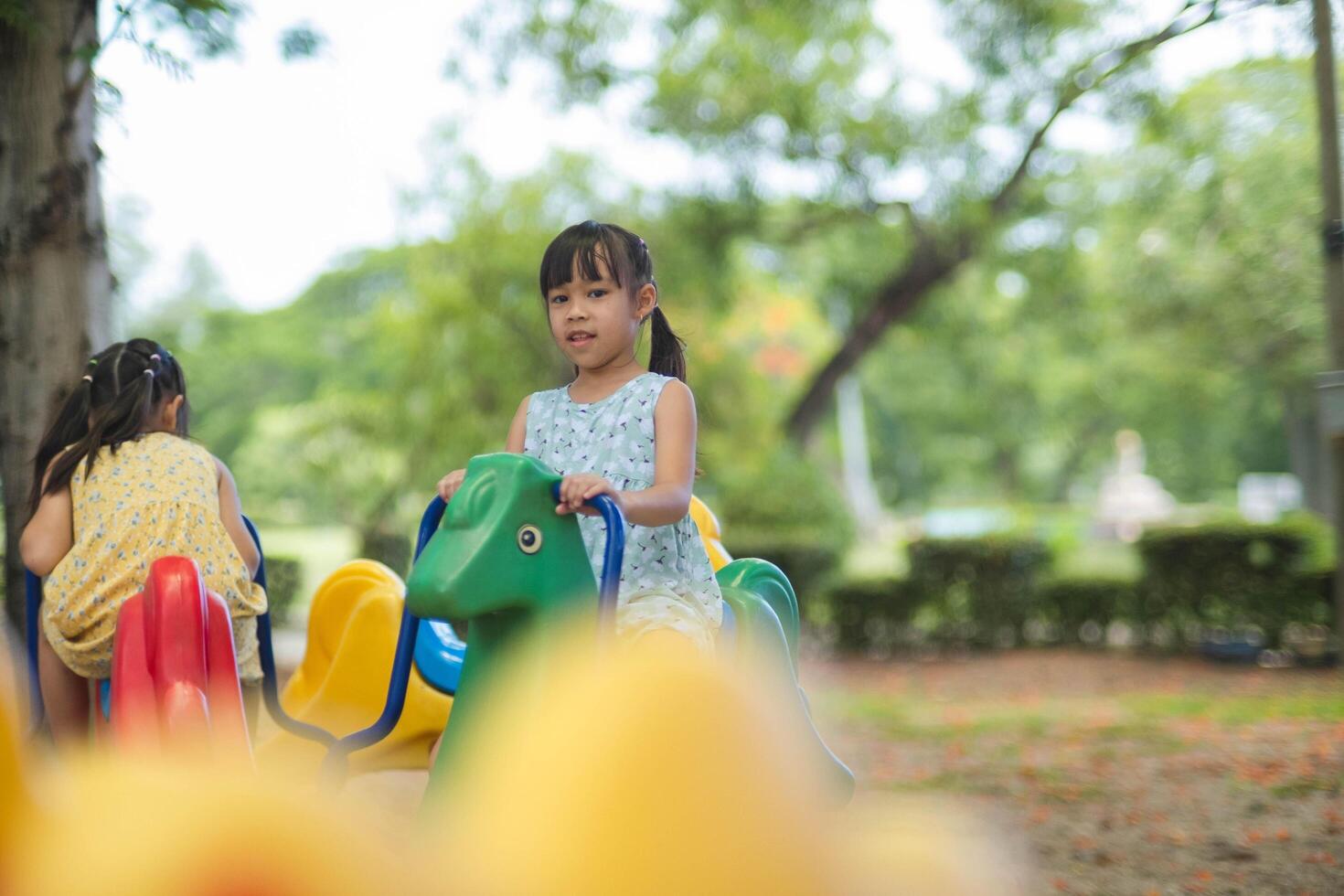 gelukkig meisje hebben pret Aan een carrousel. kinderen spelen Bij buitenshuis speelplaats in de park Aan zomer vakantie. gezond werkzaamheid. foto