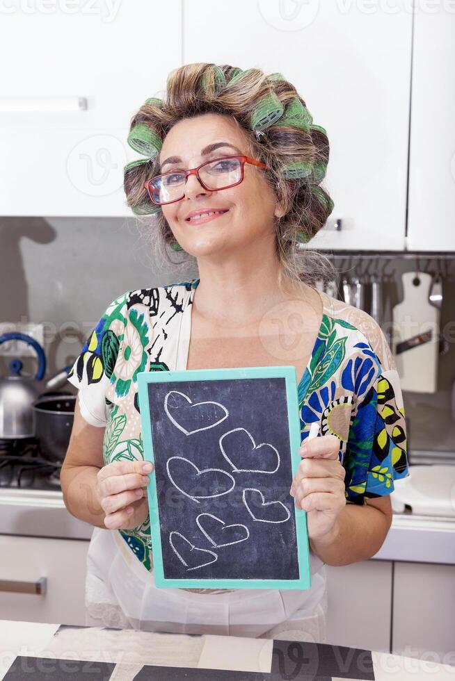 volwassen huisvrouw vrouw met krulspelden shows een bord met harten foto