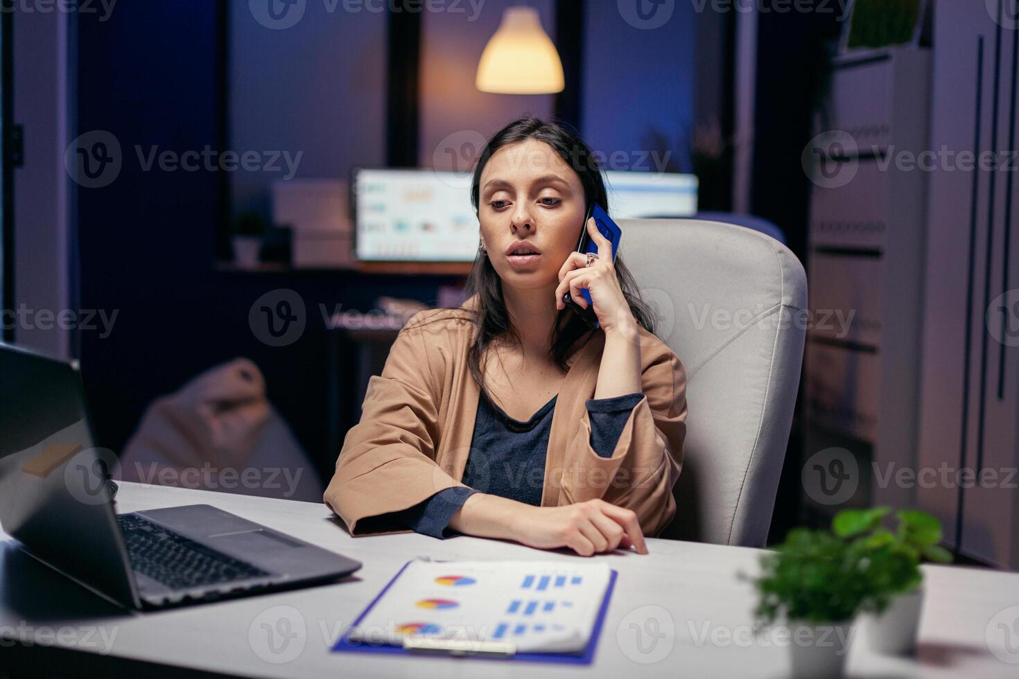 werkverslaafde manager pratend met klant over- de telefoon in de avond. vrouw ondernemer werken laat Bij nacht in zakelijke bedrijf aan het doen na een tijdje in de Cursus van telefoon telefoongesprek. foto