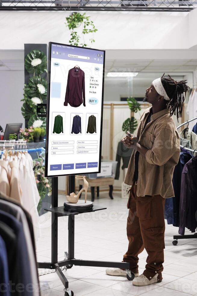 mannetje cliënt kiezen kleren Aan boodschappen doen bord kiosk onderhoud, buying mode verzameling items in kleding op te slaan gebruik makend van interactief monitor. modieus koper boodschappen doen voor producten, zelf bestellen. foto