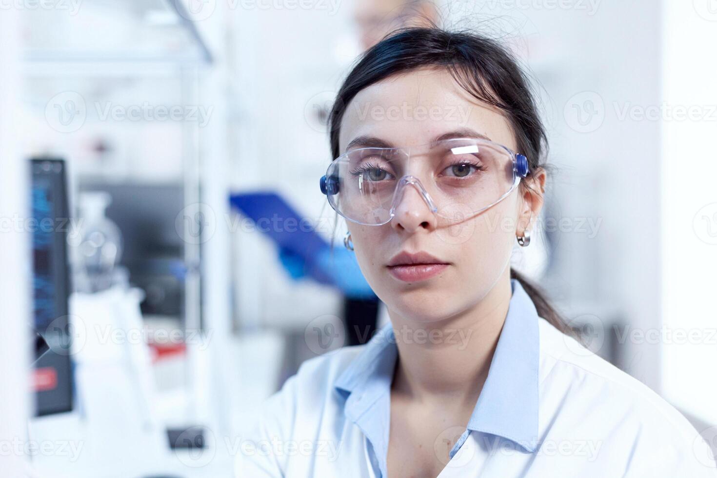 dichtbij omhoog portret van virus onderzoeker in wetenschappelijk laboratorium op zoek Bij camera. chemicus vervelend laboratorium jas gebruik makend van modern technologie gedurende wetenschappelijk experiment in steriel omgeving. foto