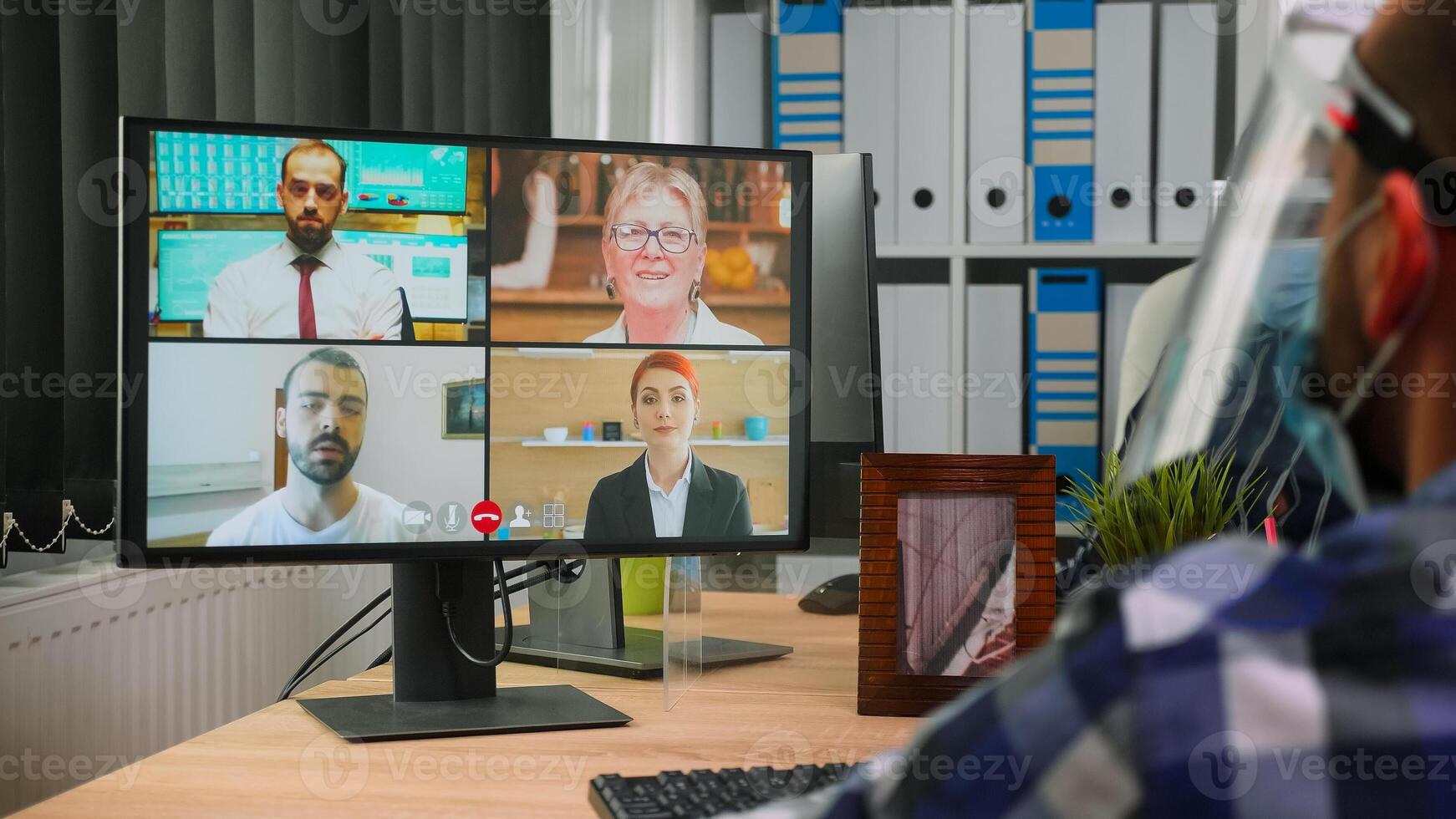 terug visie van bedrijf Mens in rolstoel pratend naar collega's over plan in video conferentie vervelend vizier in nieuw normaal kantoor. geïmmobiliseerd freelancer werken in bedrijf met inachtneming van sociaal afstand foto