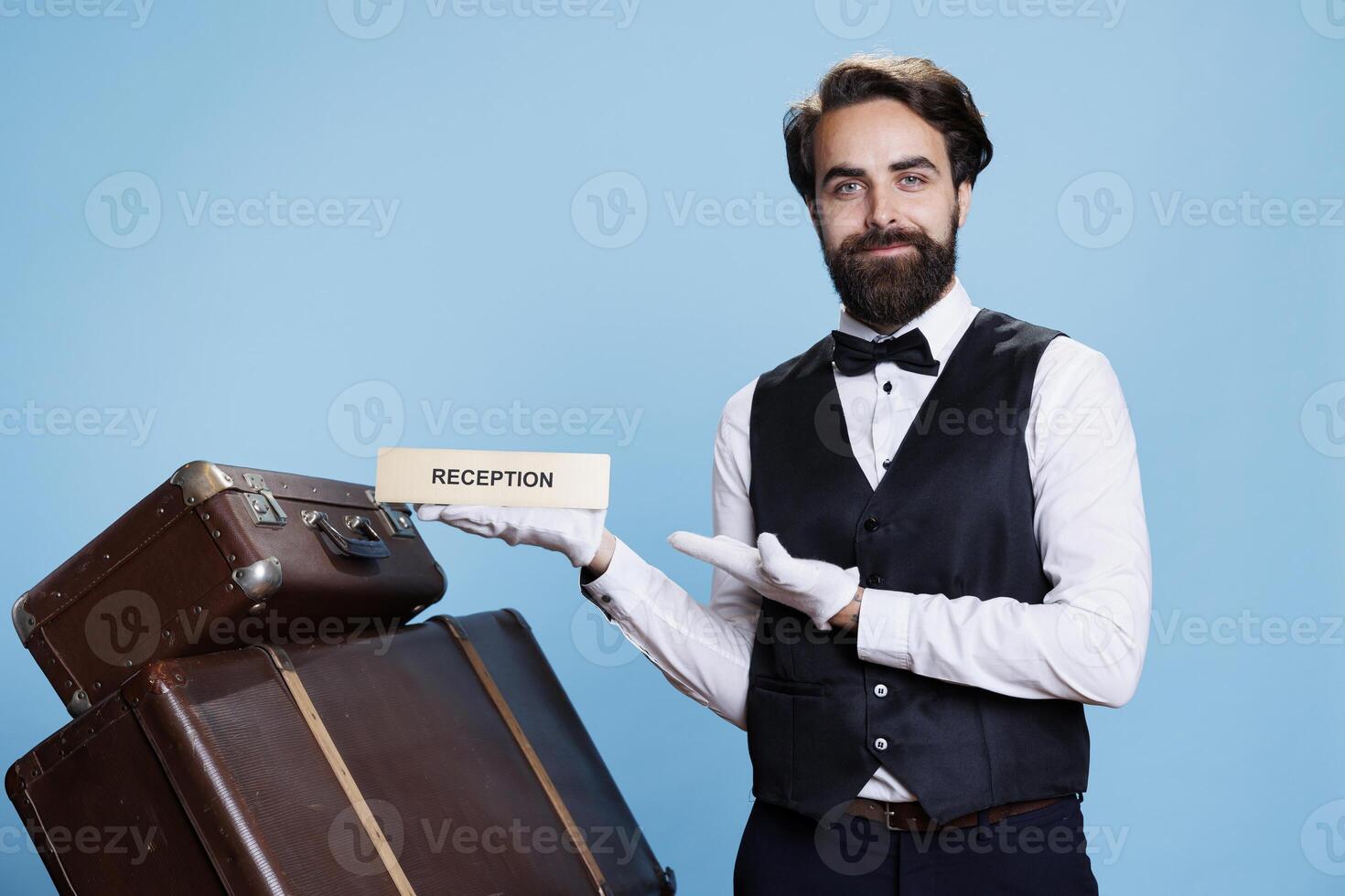 loopjongen houdt ontvangst teken Aan camera, wijzend op richting voor gasten aankomen Bij hotel. professioneel werknemer werken in gastvrijheid industrie toepassingen voorkant bureau logo, toerisme. foto