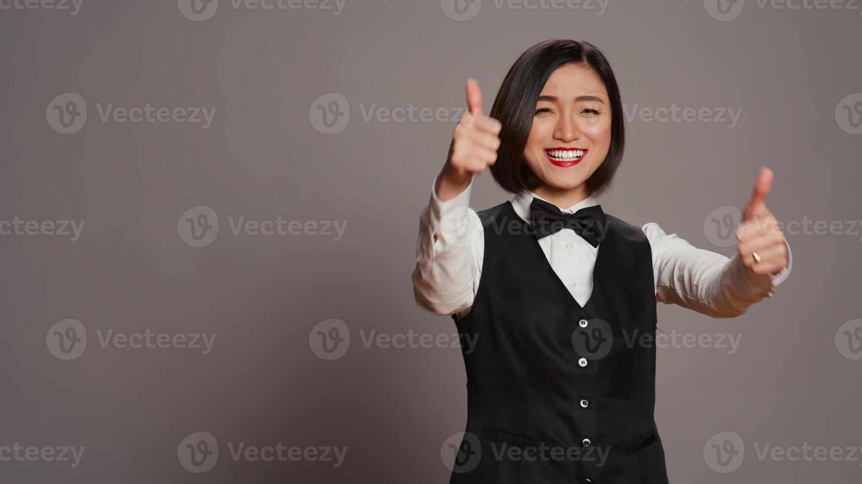 Aziatisch ontvangst personeel aan het doen duimen omhoog symbool Aan camera, tonen goedkeuring en positief teken over- grijs achtergrond. hotel receptioniste geven Leuk vinden en Oke gebaar, tonen overeenkomst. camera b. foto