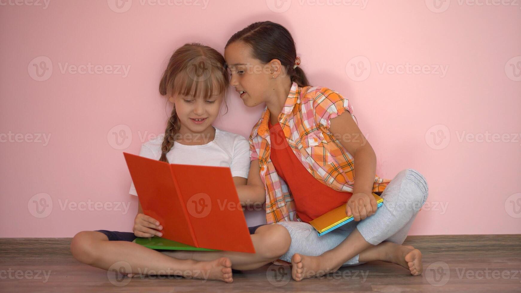 weinig meisjes lezing een boek in leven kamer. slim schoolmeisjes aan het doen hun huiswerk na school. onderwijs en afstand aan het leren voor kinderen. thuisonderwijs gedurende quarantaine. blijven Bij huis amusement. foto