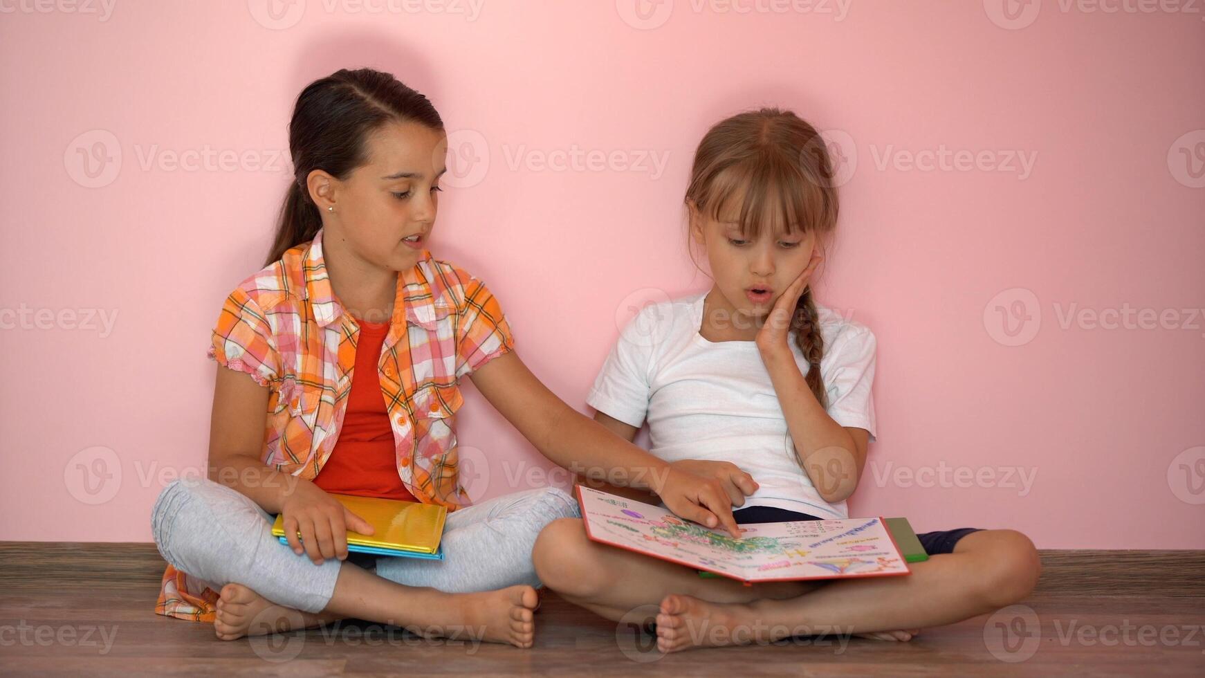 weinig meisjes lezing een boek in leven kamer. slim schoolmeisjes aan het doen hun huiswerk na school. onderwijs en afstand aan het leren voor kinderen. thuisonderwijs gedurende quarantaine. blijven Bij huis amusement. foto